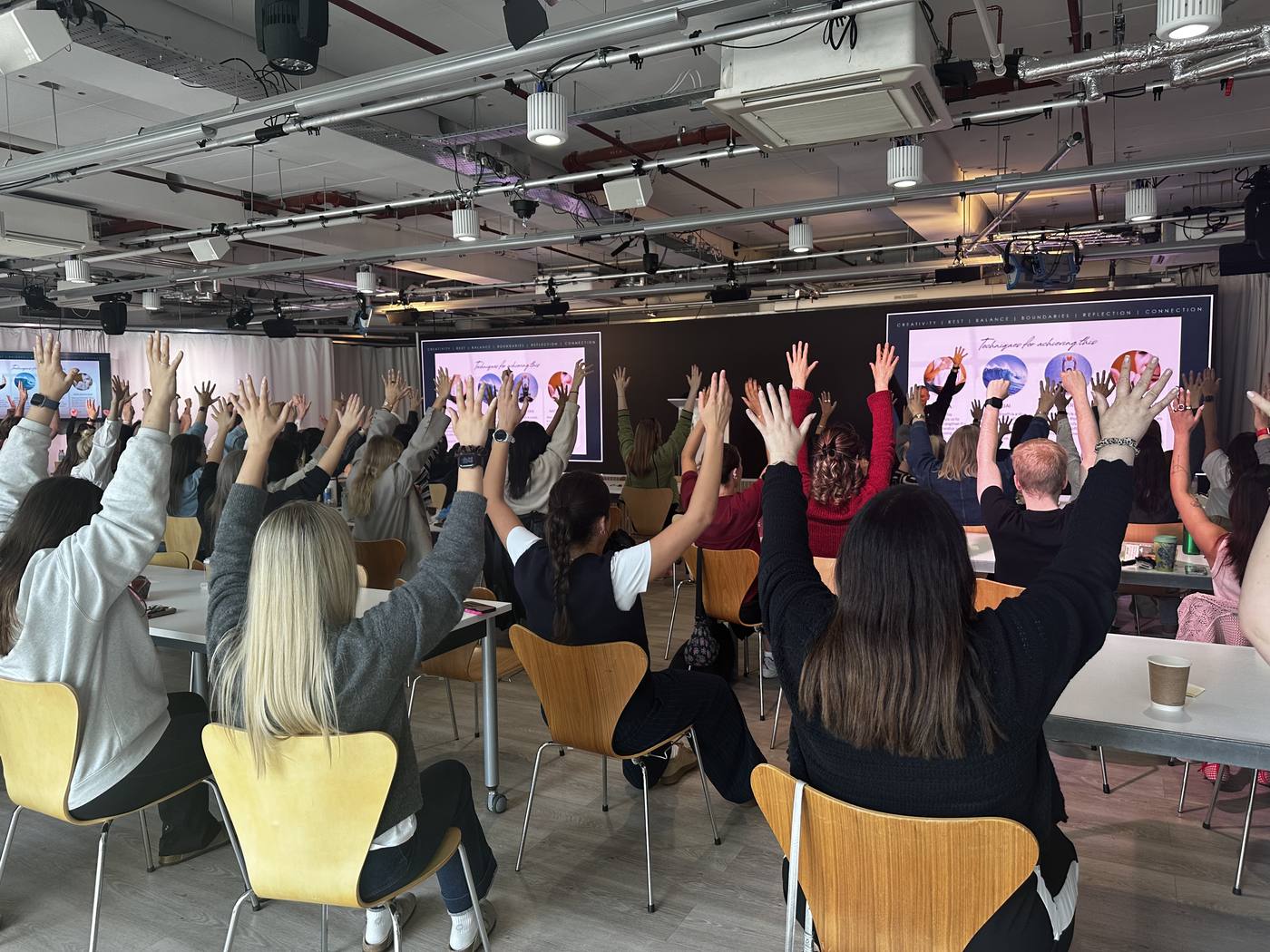 A room of attendees with hands raised during a Human Performance Programme session